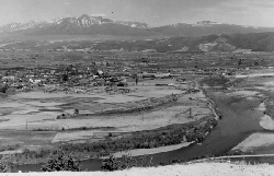 高台から写した十勝岳連山を背景にした富良野市街地全体の白黒写真