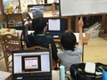 パソコンの前で子供が教わっている様子の画像